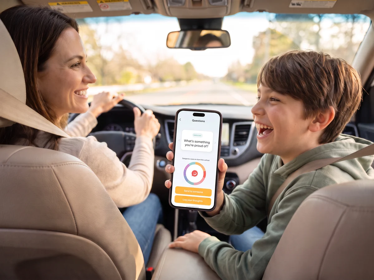 On a drive, a boy in the passenger seat laughs as he reads a Pick One question to his mum, who is driving